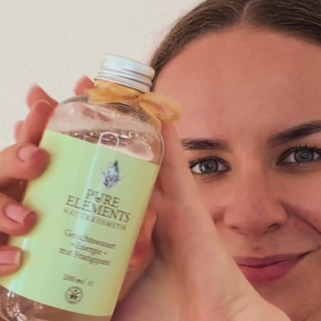 Eine Frau präsentiert das Gesichtswasser •Energie• mit Frangipani von Pure Elements Naturkosmetik. Während des gesamten Videos lächelt sie strahlend. Sie zeigt die elegante Flasche, schüttelt das Gesichtswasser sorgfältig auf ein Abschminkpad und reinigt anschließend ihre Gesichtshaut mit sanften, kreisenden Bewegungen. Ihre entspannte Mimik und positive Ausstrahlung betonen die wohltuende Wirkung der Anwendung. Die Pflege wirkt erfrischend, hautberuhigend und duftet angenehm exotisch.