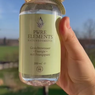 Video zeigt Gesichtswasser Energie mit Frangipani von Pure Elements in 200 ml Glasflasche. Das Produkt wird in der Hand gehalten und leicht geschüttelt, um die sichtbaren echten Bergkristalle im Inneren hervorzuheben. Die Kristalle bewegen sich im Wasser und unterstreichen die besondere energetische Qualität der veganen, tierversuchsfreien Naturkosmetik. BDIH-zertifiziert, glutenfrei, Made in Germany.